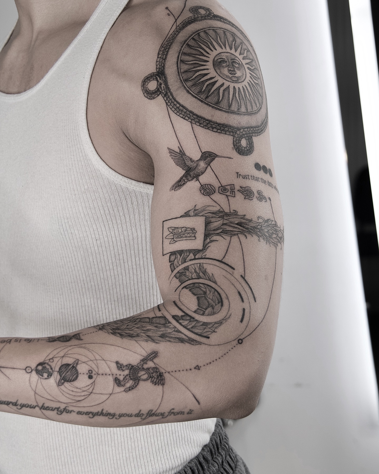 Blackwork sun and moon tattoo with hummingbird and celestial motifs on the arm